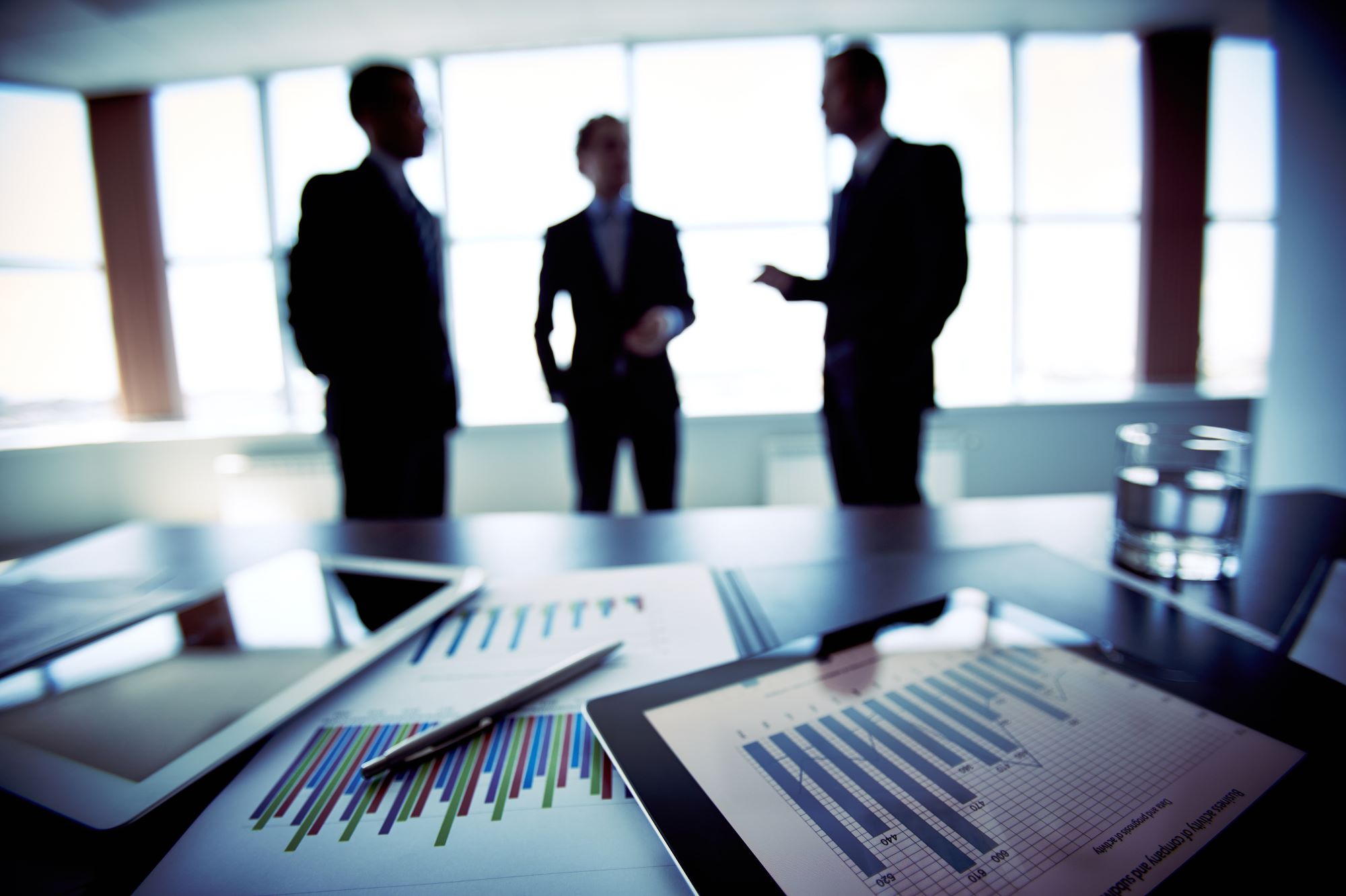 3 professionals shown in a meeting with charts and ipads with analytics data