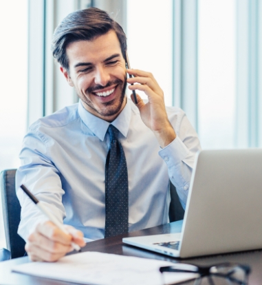 young professional shown in a shirt and tie talking on a phone and looking at a laptop