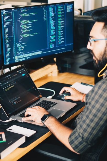 young coder working on coding with a laptop and computer pictured on a desk